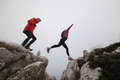 trail runner couple jumping over a cliff and running to a rocky mountain top in the early morning - PhotoDune Item for Sale