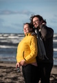 A couple stands embraced on a sandy beach on a chilly autumn day, the serene ocean stretching behind - PhotoDune Item for Sale