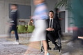 A businessman in a wheelchair navigating through a busy office, surrounded by his colleagues who are - PhotoDune Item for Sale