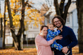 On a sunny autumn day in the park, a mother and father lovingly embrace their young son, sharing - PhotoDune Item for Sale