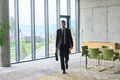A determined businessman in a black suit confidently walks through the office, embodying - PhotoDune Item for Sale