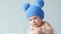 A calm newborn baby in a blue hat with pompoms looks into the camera. - PhotoDune Item for Sale