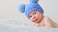 A happy newborn baby in a blue hat with pompoms looks into the camera. Cheerful White kid. - PhotoDune Item for Sale