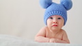A happy newborn baby in a blue hat with pompoms looks into the camera. - PhotoDune Item for Sale